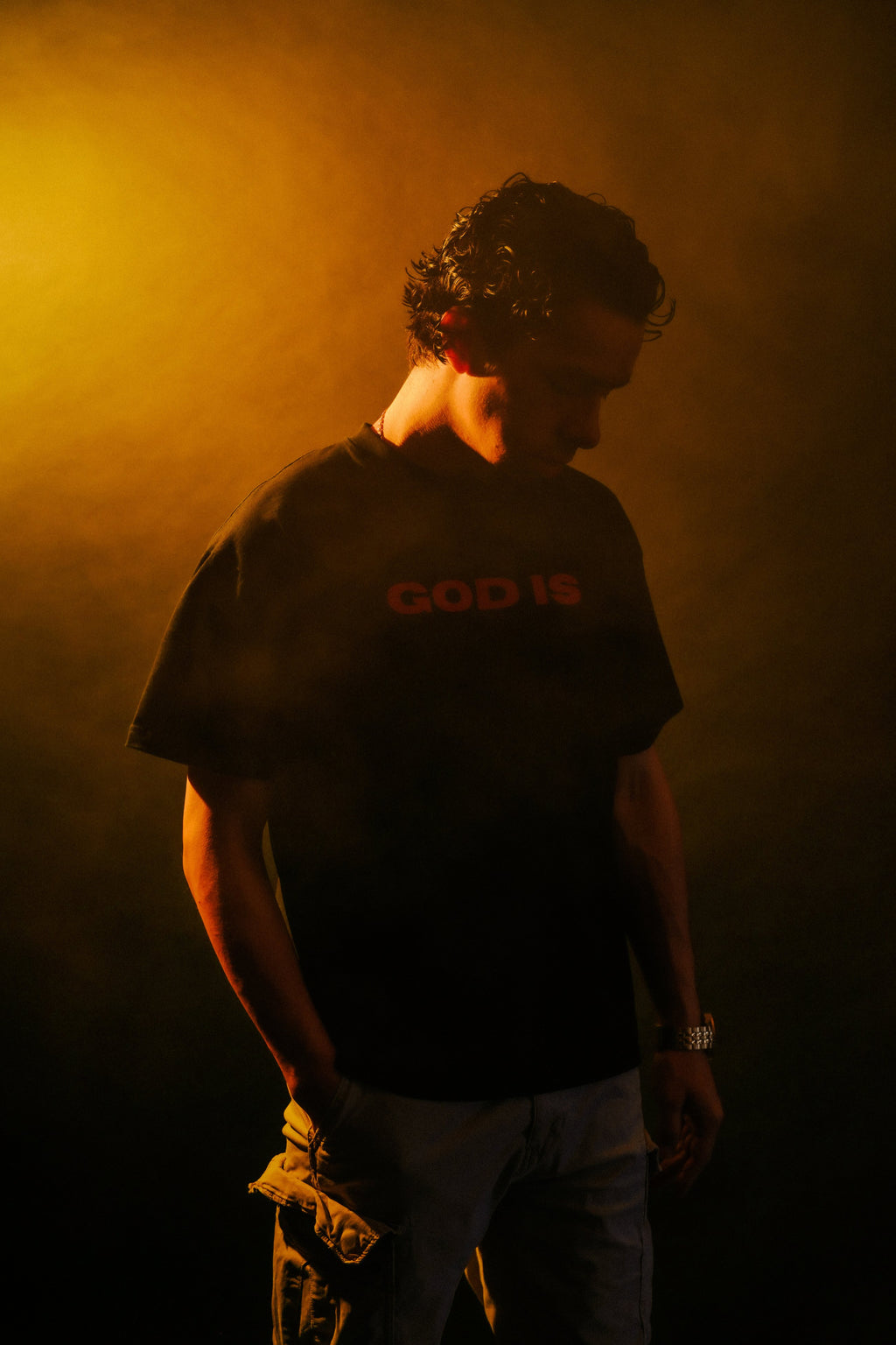 Man wearing GOD IS Christian tee, side profile, warm lighting