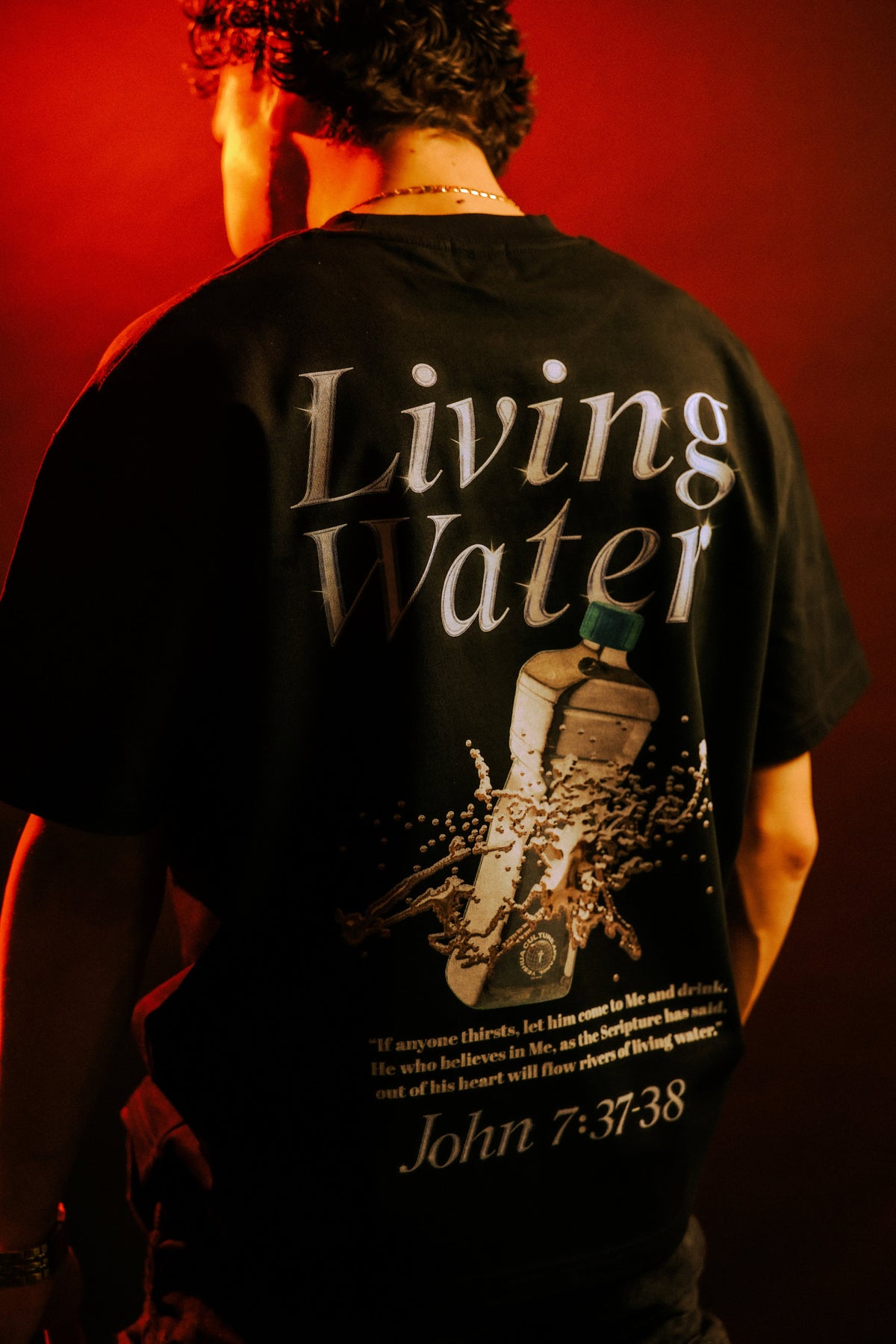 Man wearing LIVING WATER Christian tee, back graphic in red-lit studio