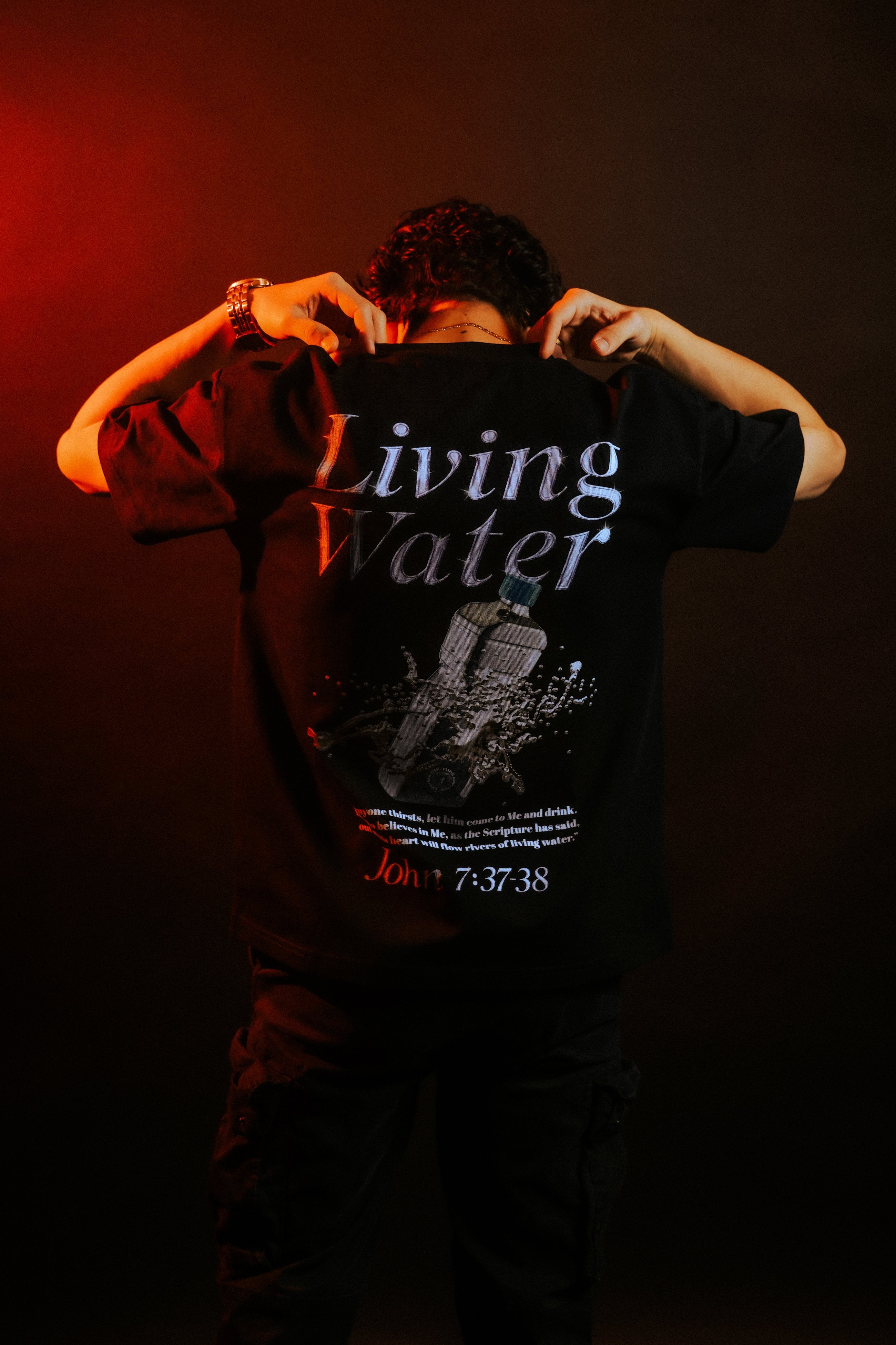 Man in LIVING WATER Christian streetwear tee, arms raised, red-lit lifestyle shot