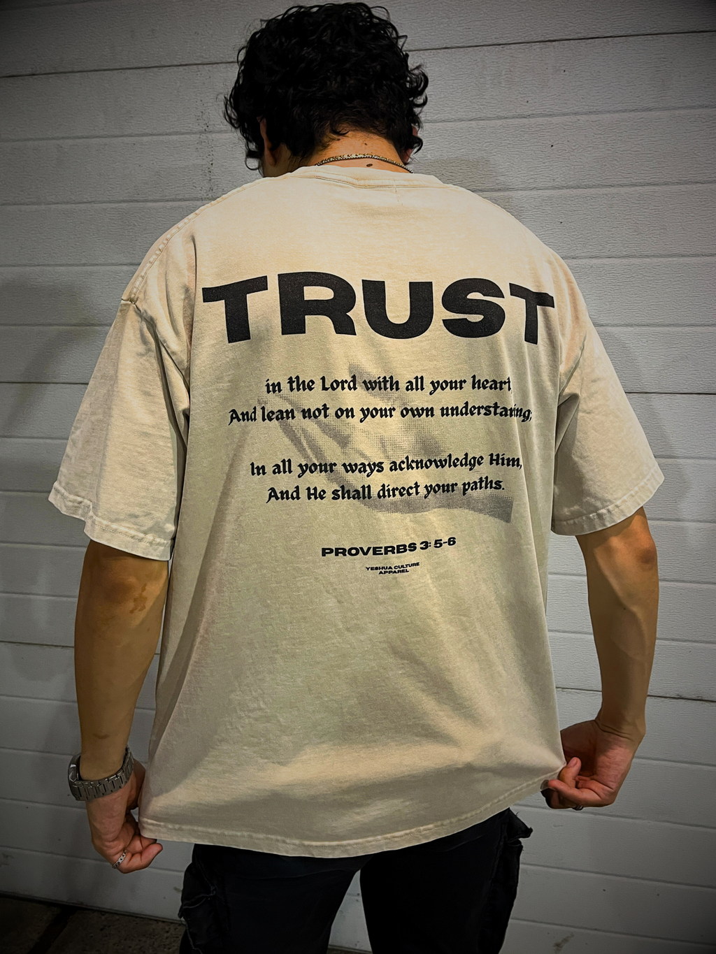 TRUST Oversized Christian Tee back view with Proverbs 3:5–6 verse — model holding hem, scripture clearly visible