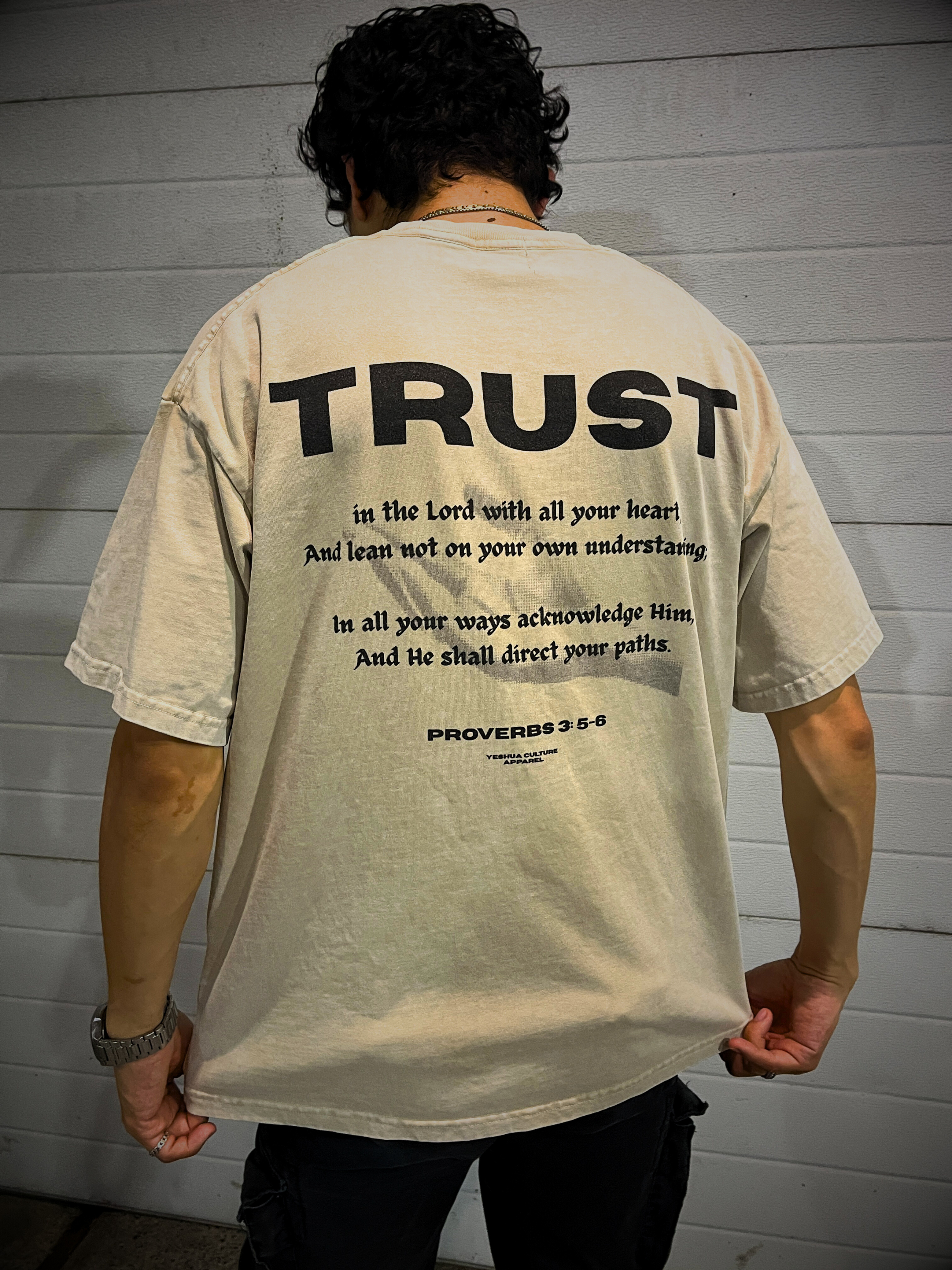 TRUST Oversized Christian Tee back view with Proverbs 3:5–6 verse — model holding hem, scripture clearly visible