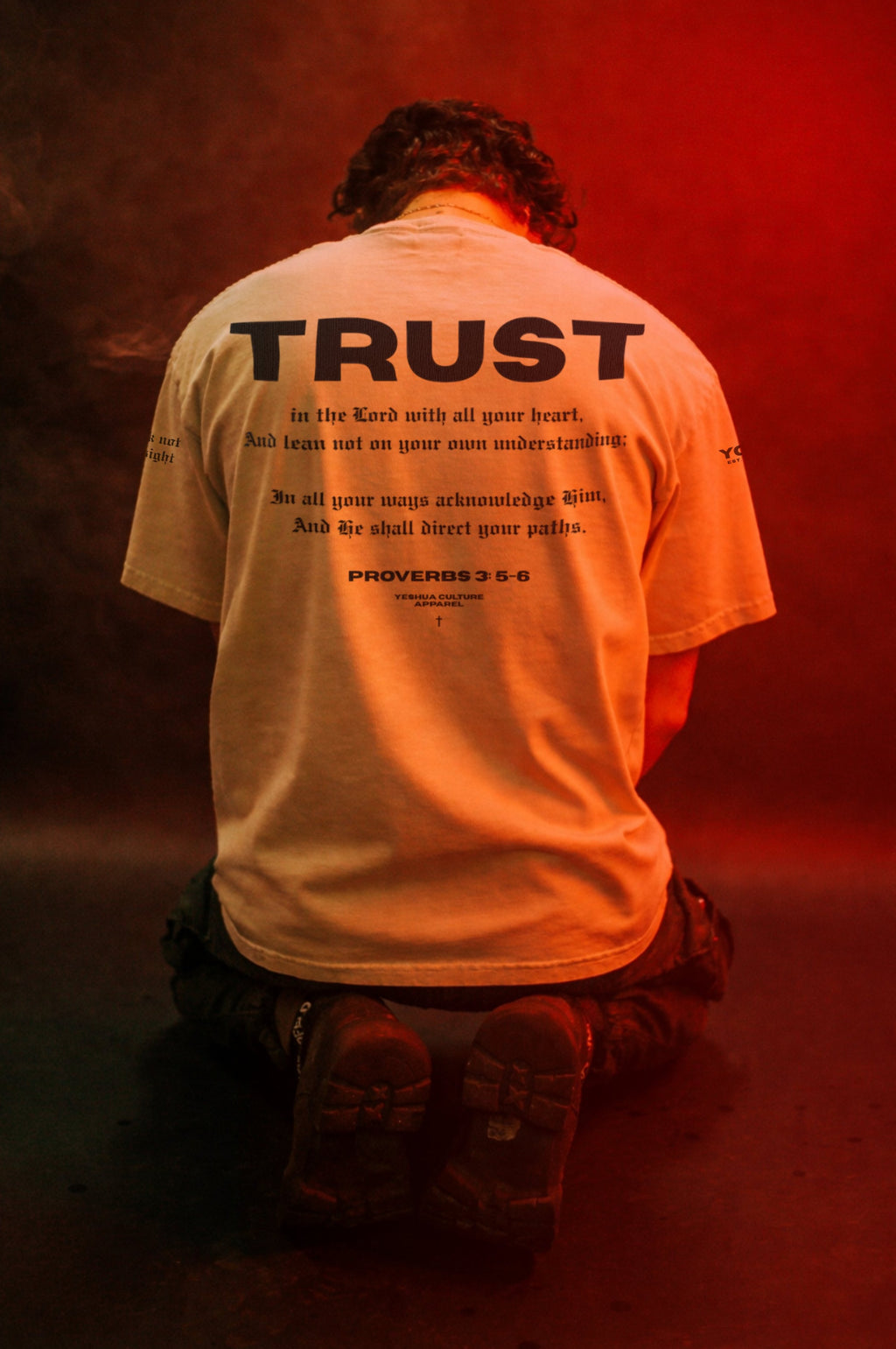 Back view of man wearing TRUST tee, kneeling pose, red-lit lifestyle shot